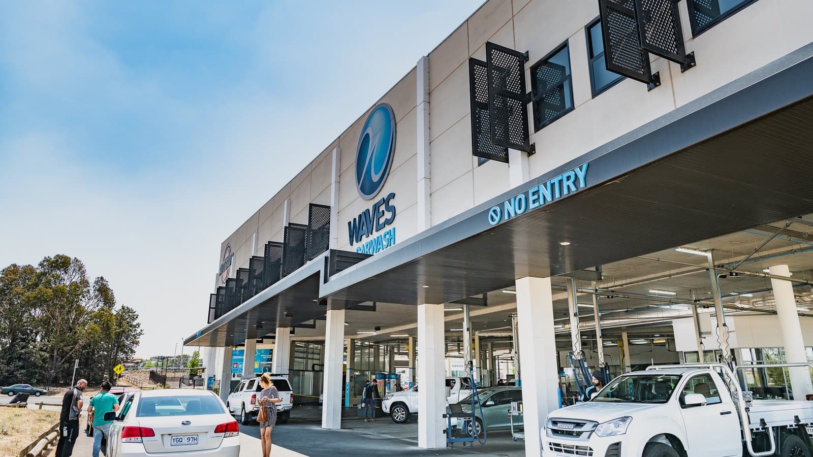 The forecourt of a Waves car wash, with cars queued under the branded canopy